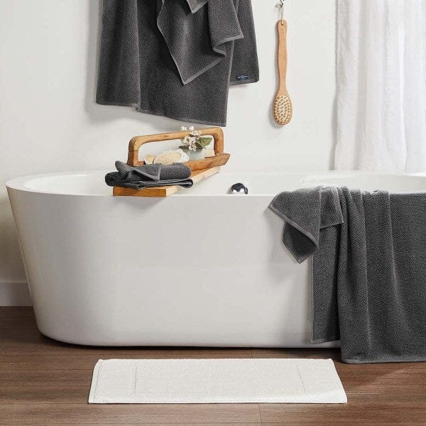 Freestanding tub with Lotus towels in charcoal shown draped over tub and hanging above it. A white Lotus bath mat is next to the tub in a luxurious bathroom setting.