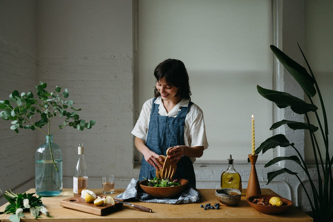 Woman preparing salad for a dinner party on a large wood table