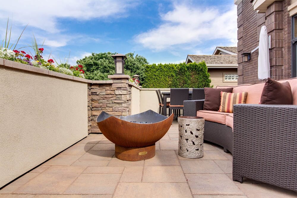 modern patio decor that includes a minimalist, curved firepit, wicker recliners, and a simple concrete patio with a wall and planter on it