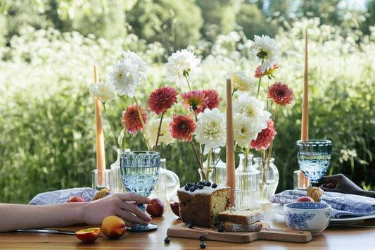 Outdoor summer table setting with blue glassware, fresh flowers, candles, and cake for al fresco entertaining