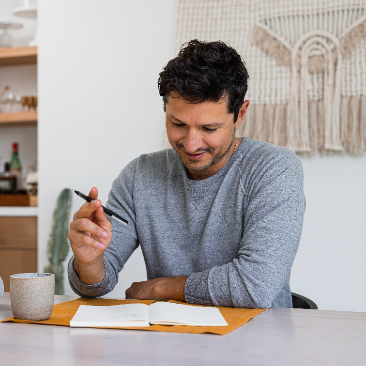 Man sits at table drinking coffee and writing in notebook