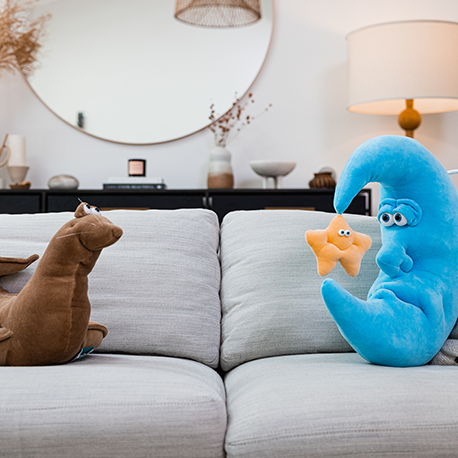 Stuffed brown seal and blue moon with star sit on a couch