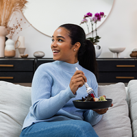 Woman eating salad and smiling on a couch