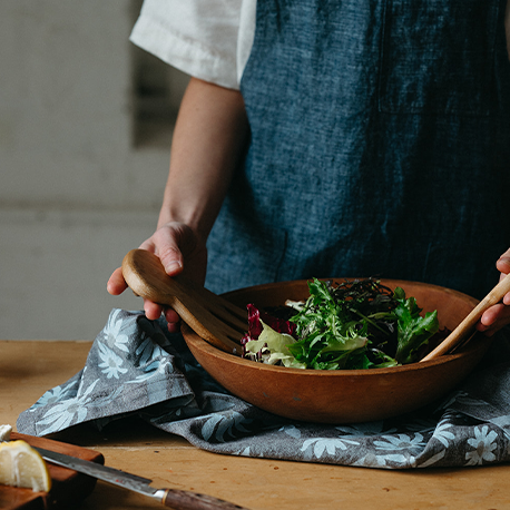 Woman tosses salad in wooden bowl